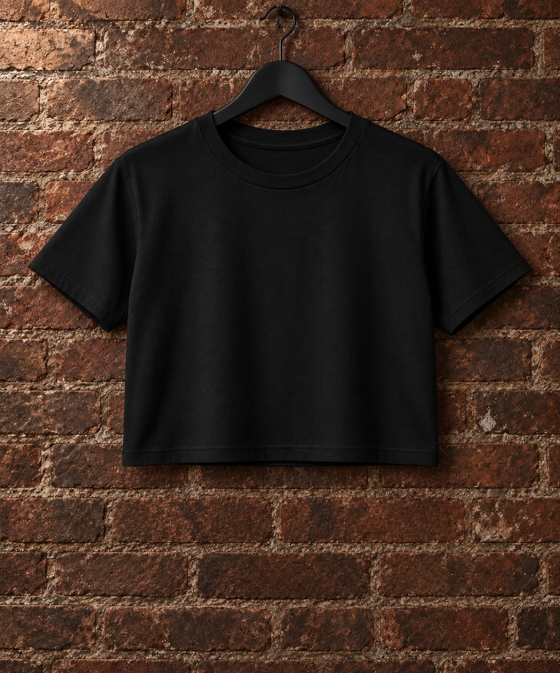 Remera crop de mujer negra colgada sobre pared de ladrillos
